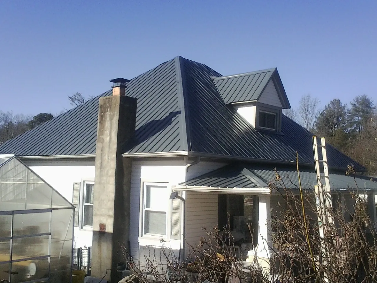 Dark blue standing seam metal roof on a white farmhouse with dormer — Slate & Tile Roof Repair by Roofing Brothers in Mullins