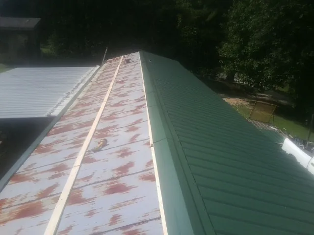 Old rusted panels beside newly installed green metal roofing — Wind Damage Roof Repair by Roofing Brothers in Mullins