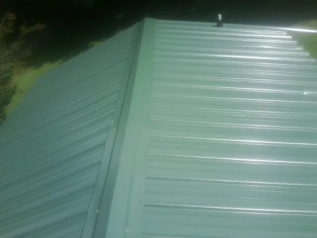 New green metal panels meeting at the ridge of a roof — Flat Roof Repair work by our crew in Mullins