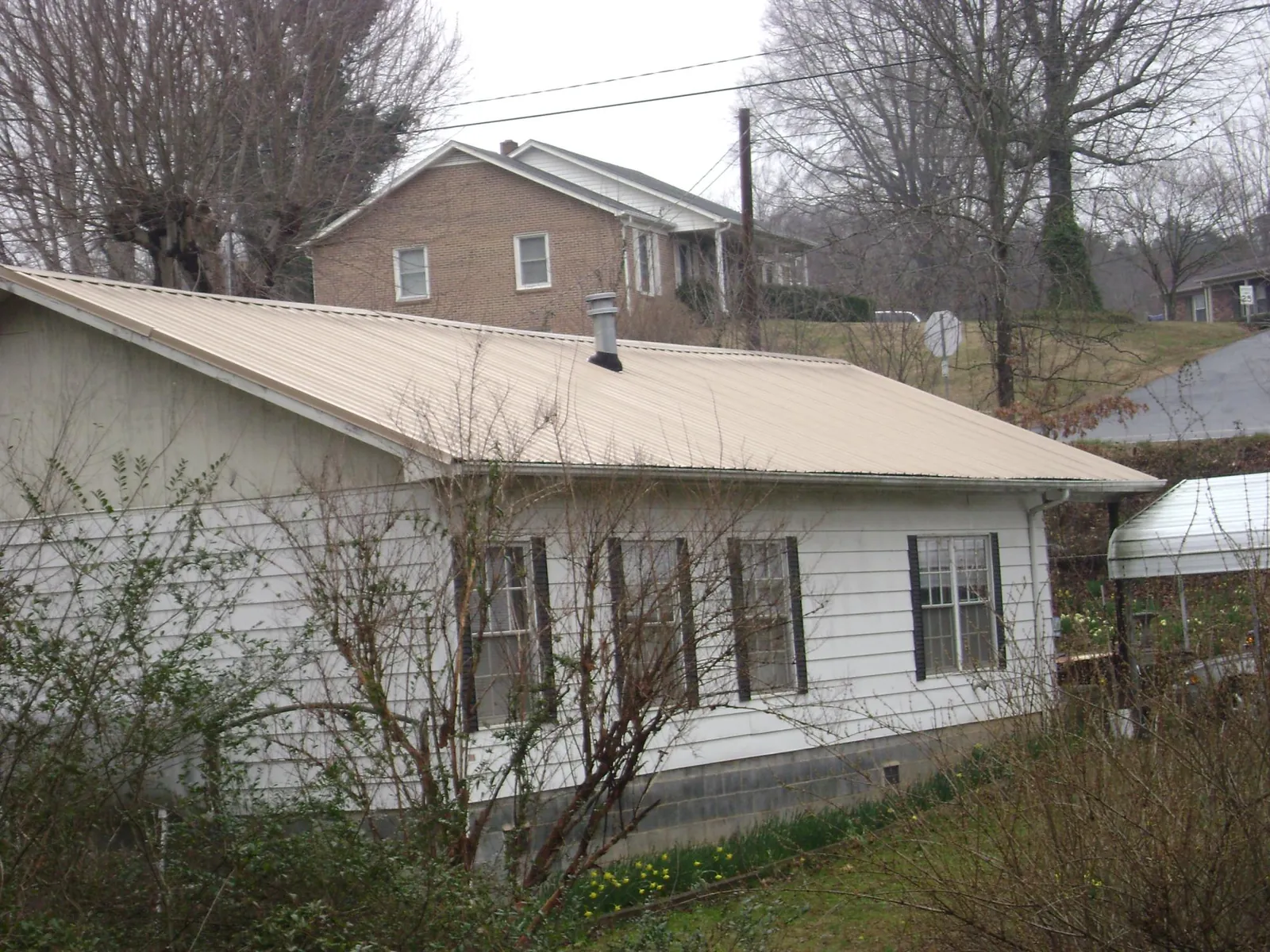 Tan metal roof on a white sided house set into a hillside — Commercial Roofing by Roofing Brothers in Mullins