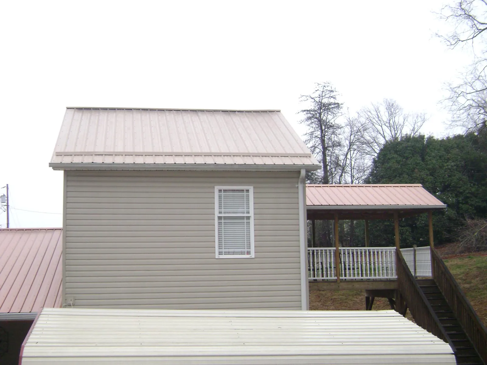 Tan metal roofs on a two story addition and attached porch, from a Roof Replacement job in Mullins